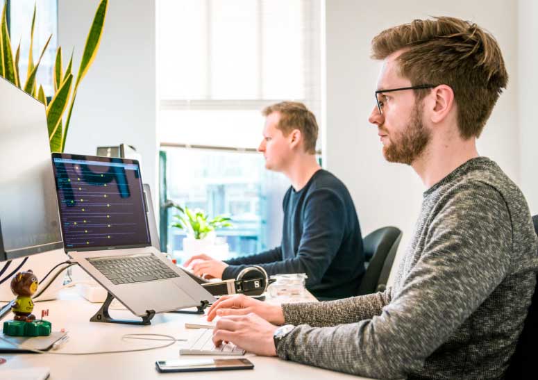 Two professionals working at desks with laptops in a modern office.